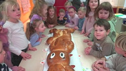 Kinder sind rings um den Hefehasen verteilt und warten darauf, endlich naschen zu können.