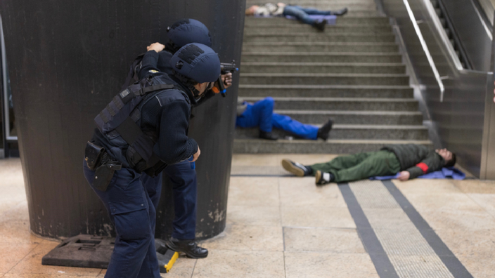 Zwei bewaffnete Polizisten blicken auf eine Treppe, auf der Menschen liegen.