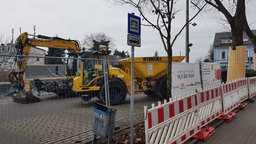 Hinter einem Bauzaun stehen schwere Arbeitsgeräte