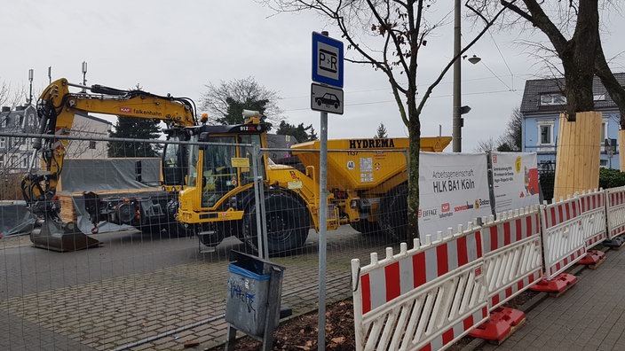 Hinter einem Bauzaun stehen schwere Arbeitsgeräte