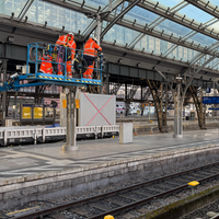 Arbeiter in orangenen Anzügen stehen auf einer Hebebühne neben den Gleisen am Hauptbahnhof.