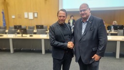 Der amtierende Bürgermeister Uwe Richrath steht im Ratssaal Leverkusen neben seinem CDU-Kontrahenten Stefan Hebbel, die beiden reichen sich die Hand