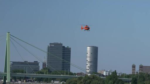 EIn roter Helikopter fliegt über den Rhein in Köln.