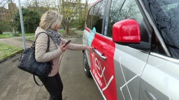 Ein Frau mit Handy in der Hand will die Tür eines Kleinbusses öffnen