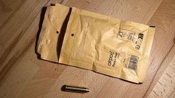 Ein Laserpointer in Patronenoptik und ein geöffneter brauner Briefumschlag liegen auf einem Tisch.