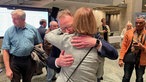 Torsten Burmester umarmt Henriette Reker in einem großen Saal mit Menschen drumherum. Reker steht mit dem Rücken zur Kamera.