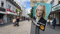 Ein ramponiertes Wahlplakat hängt an einer Laterne. Darauf zu sehen ist eine mittelalte Frai mit blonden Haaren.