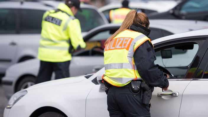 Zwei Bundespolizisten stehen an zwei Autos und kontrollieren Papiere