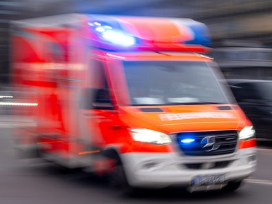 Auf dem Foto ist ein Krankenwagen der Feuerwehr mit Blaulicht, der über eine Straße fährt.