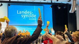 Mitglieder der Evangelischen Landessynode in Bonn heben ihre Stimmzettel hoch.
