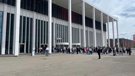 Das Gebäude der Koelnmesse von außen, davor lange Schlangen von Besuchenden.