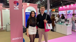 Ein Paar steht in einer Halle der Beauty Messe in Düsseldorf, hinter ihnen rosa Teppich und ein rosa Stand