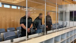 Angeklagter und zwei Beamte im Gerichtsaal