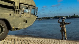 Ein Militärfahrzeug am Rheinufer, daneben ein Soldat in Uniform