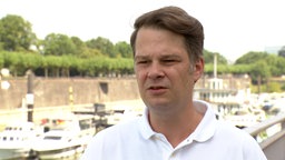 Ein mittelalter Mann mit gräulichen Schläfen im weißen Polo-Hemd an einem Hafen