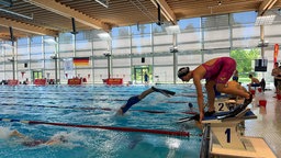 Eine Schwimmerin steht mit Schwimmhaube und Flossen auf einem Startblock