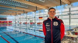 Ein Mann steht in Trainingsklamotten vor einem Schwimmbecken
