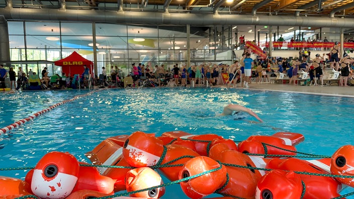Ein Mann schwimmt in einem Schwimmbecken, im Vordergrund liegen mehrere Rettungspuppen