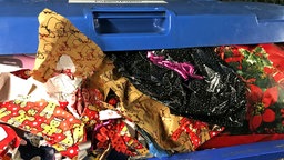 Eine große Papiermülltonne, aus der buntes Geschenkpapier quillt