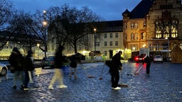 Zu sehen sind Menschen mit Besen, die den Platz reinigen.