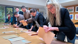 Zu sehen sind mehrere Wahlhelfer*innen, die Wahlzettel sortieren.