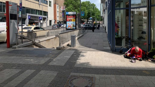 Blick auf den Eingang der U-Bahn-Station Appellhofplatz. Daneben ein Obdachloser.