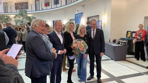 Der neuer Landrat Klaus Gootens steht in einem Saal in der Mitte einer Gruppe von Personen. Eine von ihnen hält einen Blumenstrauß.
