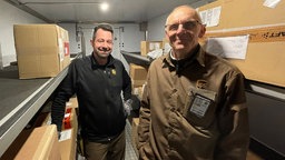 Paketzusteller Guido Hemmersbach steht mit seinem Kollegen im Zustellwagen.