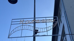Zu sehen ist ein leuchtender Schriftzug, welcher an einer Laterne befestigt ist