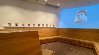 Ein hölzerner Raum mit Projektionen von Opfern des Nationalsozialismus an der Wand