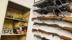 Langwaffen in Wandregal, geöffneter Schrank mit Paketen und Kisten