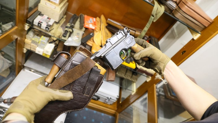 Waffe wird aus Leder- Holster gezogen, Hände mit Arbeitshandschuhen
