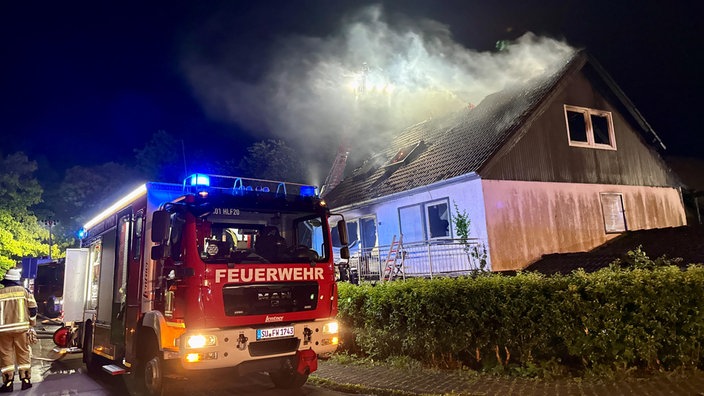 Ein Feuerwehrauto steht nachts vor einem Wohnhaus in Lohmar, aus dem weißer Rauch aufsteigt.