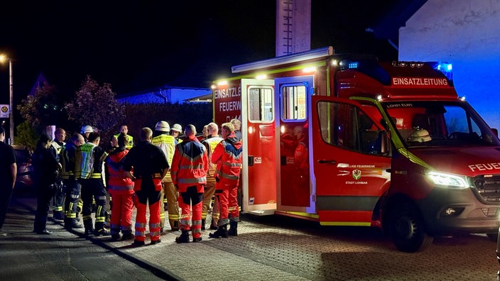 Einsatzkräfte von Feuerwehr und Rettungsdienst steheh nachts auf einer Straße vor einem Feuerwehrfahrzeug und besprechen sich.