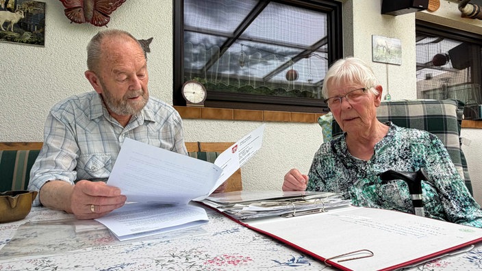 Hildburg und Georg Neumann  sitzen an einem Tisch auf ihrer Terasse und schauen Unterlagen durch.