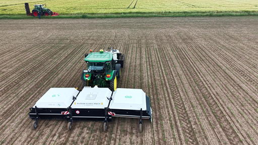 Ein großer Traktor mit einer anhängenden Maschine fährt über ein Feld.