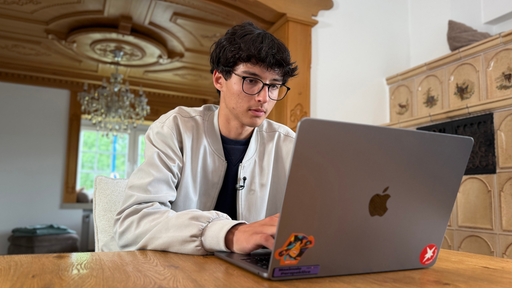 Rezan sitzt am Tisch und tippt auf seinem Apple Laptop