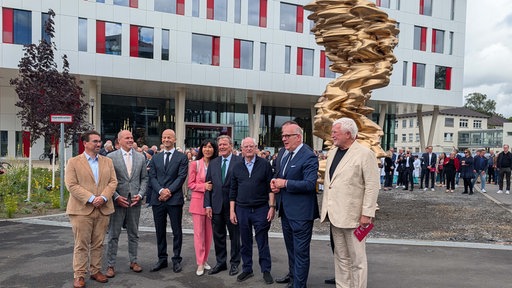 Mehrere Männer und eine Frau machen ein Gruppenfoto vor einer goldenen Skulptur.