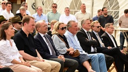 Auf dem Foto sind Menschen, die auf Stuhlreihen sitzen und ernst gucken, darunter der Düsseldorfer Oberbürgermeister Stephan Keller.