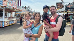 Auf dem Foto sind eine Frau mit asiatischem Aussehen und ein europäisch aussehender Mann, die jeweils ein Kind auf dem Arm haben.