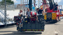 In einem Rettungskorb stehen zwei Feuerwehrmänner und zwei Zivilisten