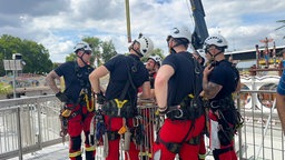 Mehrere Feuerwehrmänner stehen an einem Fahrgeschäft der Rheinkirmes Düsseldorf und besprechen den Einsatz