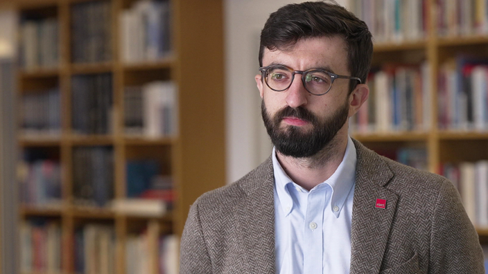 Lorenzo Scarazzato steht vor einer Bücherwand.