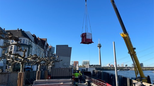 ein Kran transportiert einen Ventilator am Rhein-Ufer