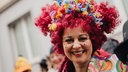 Eine Frau mit roter Perücke und bunt bemaltem Gesicht lacht in die Kamera.