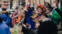 Eine Frau im bunten Federkostüm steht mit vielen anderen verkleideten Leuten am Straßenrand.