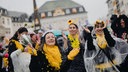 Vier Frauen in gelb-schwarzen Kostümen tanzen im Regen.