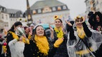 Vier Frauen in gelb-schwarzen Kostümen tanzen im Regen.