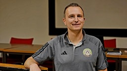 Gregor Hoffmann sitzt in Trikot-Shirt an einem Tisch und lächelt in die Kamera.