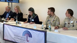 Auf dem Bild sieht man eine Pressekonferenz der Mönchengladbacher Pfadfinder. Insgesamt sitzen fünf Personen an einem Tisch. 